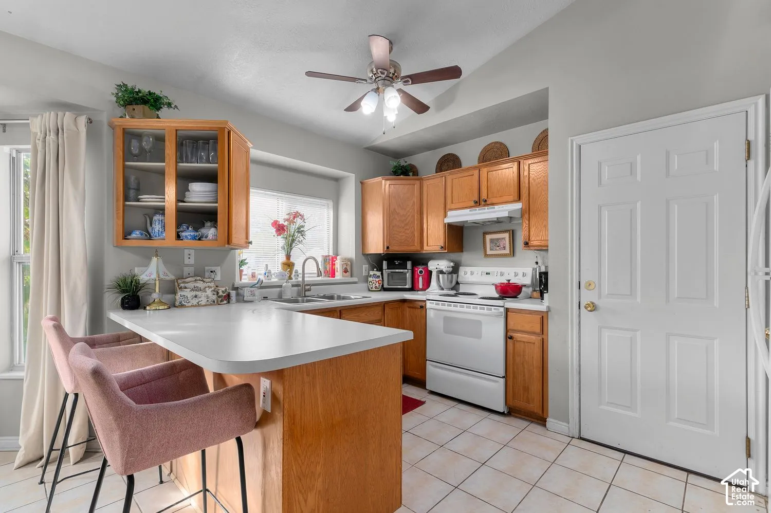 Kitchen featuring natural wood cabinetry, white countertops, ceramic tile flooring, a dual-basin sink, and a ceiling-mounted light fixture with integrated fan