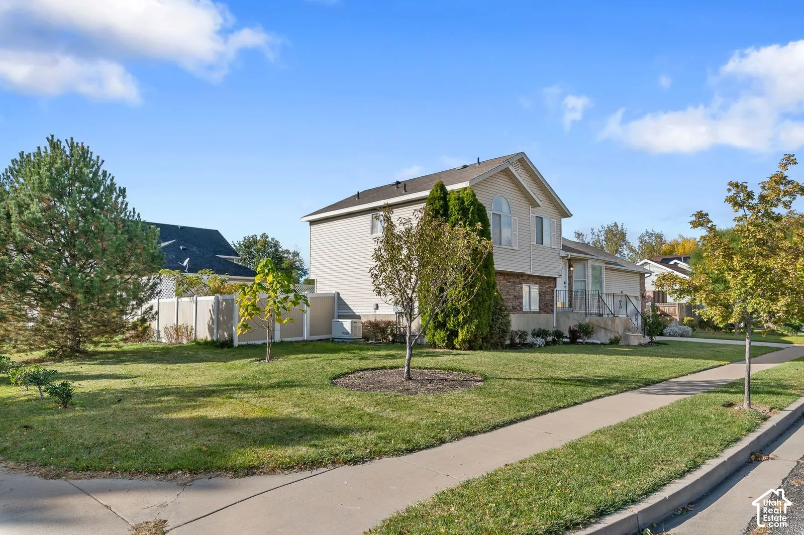 Two-story residence featuring light-colored horizontal siding, a partial stone veneer facade, an arched second-story window, a concrete driveway, and a privacy fence