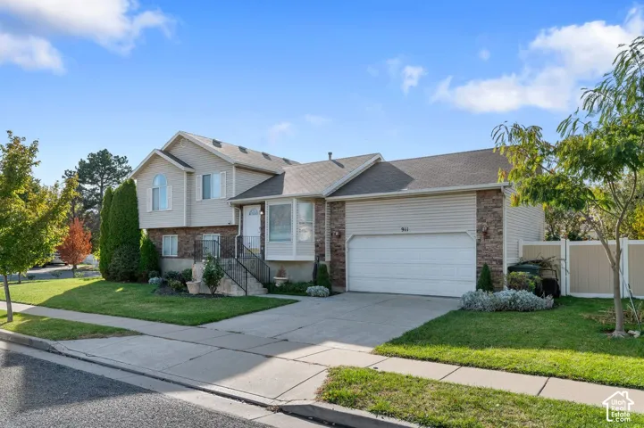 Split-level exterior featuring light-toned horizontal siding, stone veneer accents, an attached two-car garage, concrete driveway, and a manicured front lawn