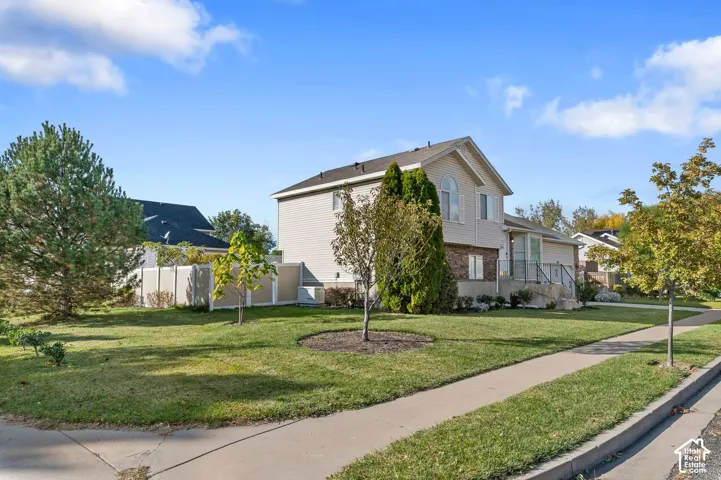 Two-story residence featuring light-colored horizontal siding, a partial stone veneer facade, an arched second-story window, a concrete driveway, and a privacy fence