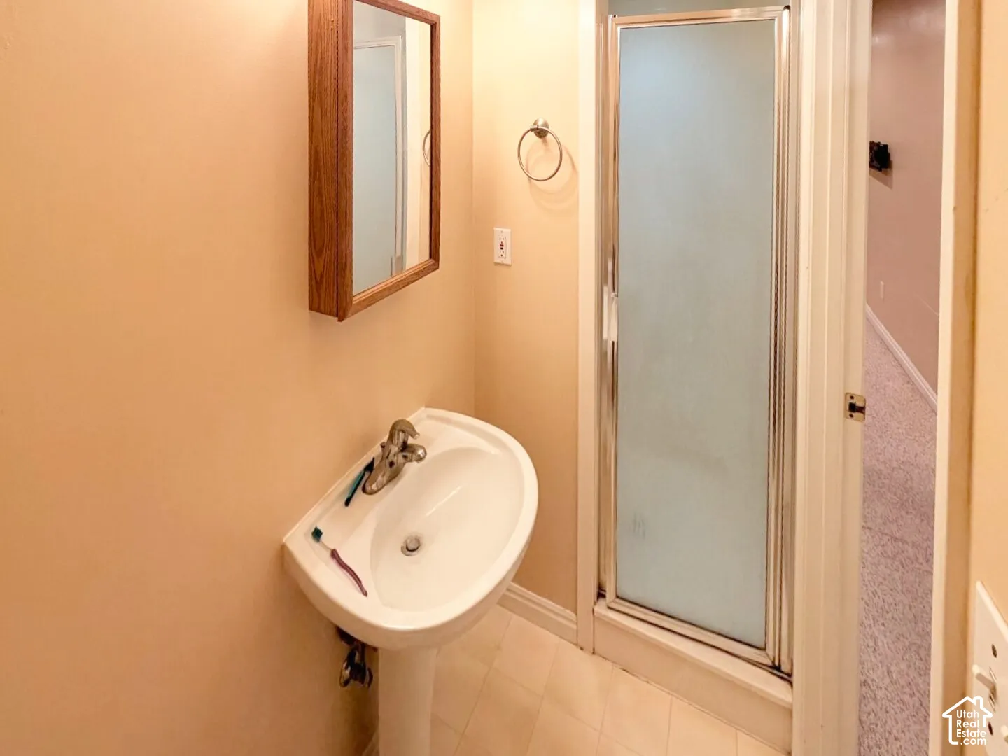 Bathroom featuring a white pedestal sink, single-handle metal faucet, wall-mounted wooden medicine cabinet, and a glass-enclosed shower stall