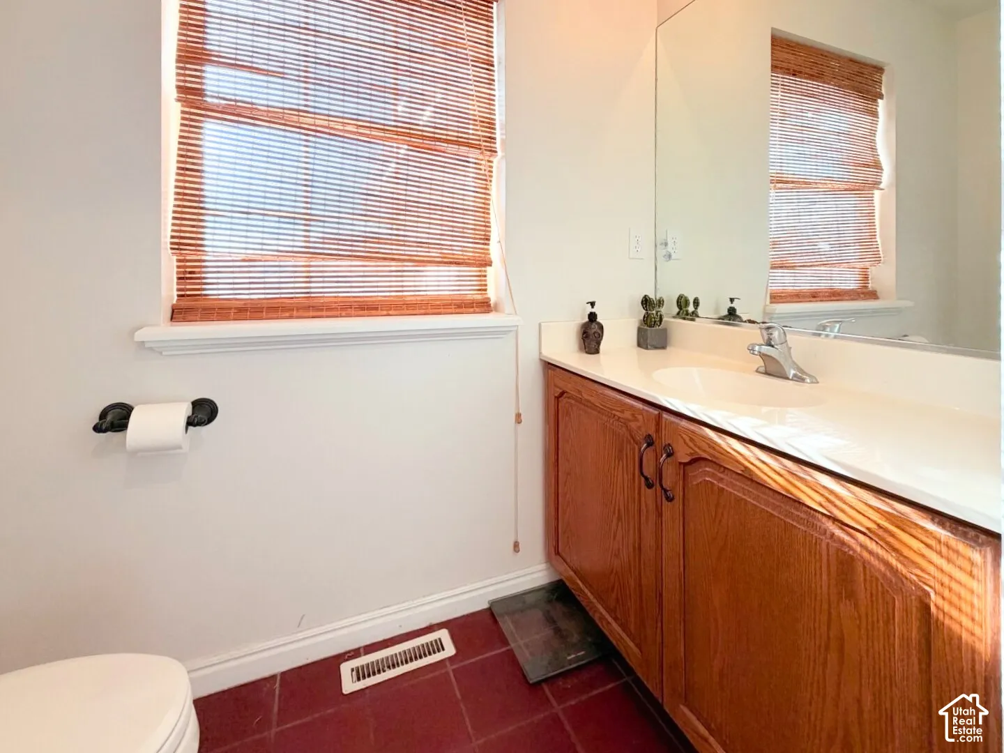 Bathroom vanity featuring wood-finish cabinetry, a white countertop with an integrated basin, a large wall-mounted mirror, and tile flooring
