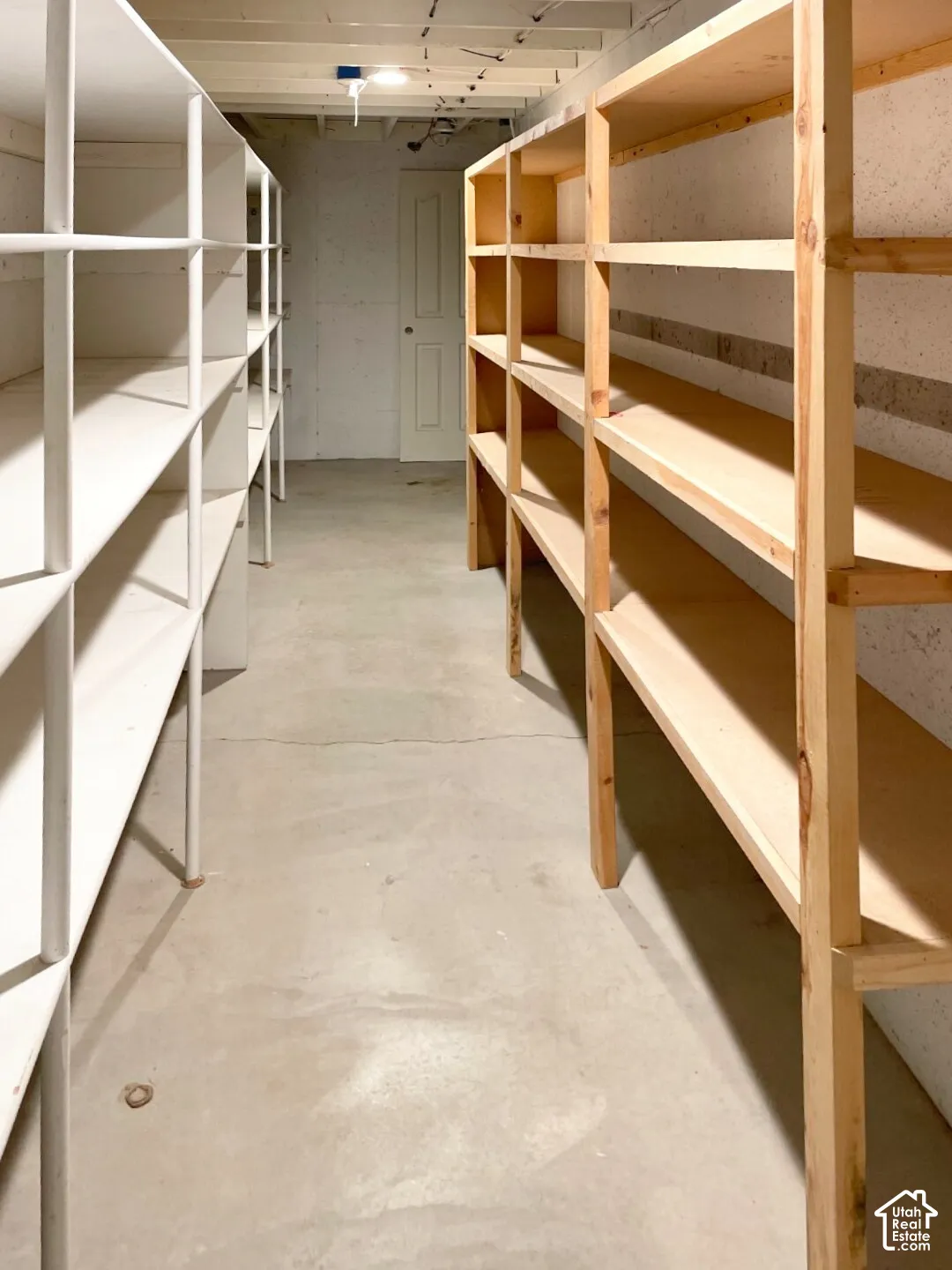 Storage area featuring concrete flooring, built-in white metal shelving, and natural wood-frame shelving