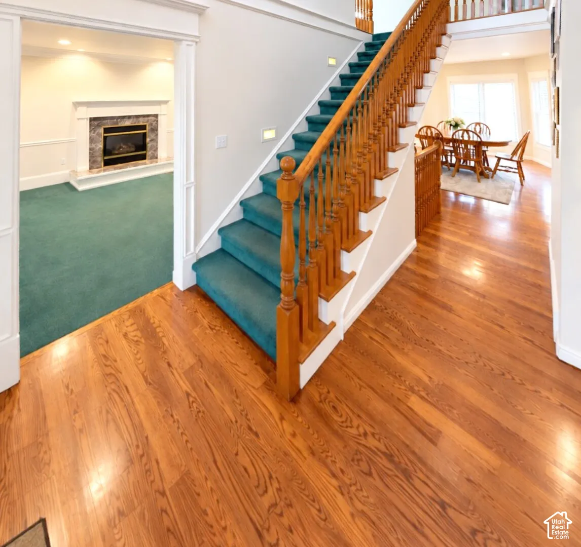 Foyer featuring wood-finish flooring, a staircase with a wooden balustrade, and a fireplace with a stone-surround mantel