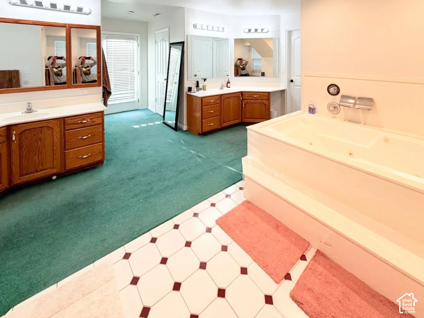 Dual vanity areas featuring wood cabinetry, white countertops, oversized wall-mounted mirrors, and geometric tile flooring with a large built-in soaking tub