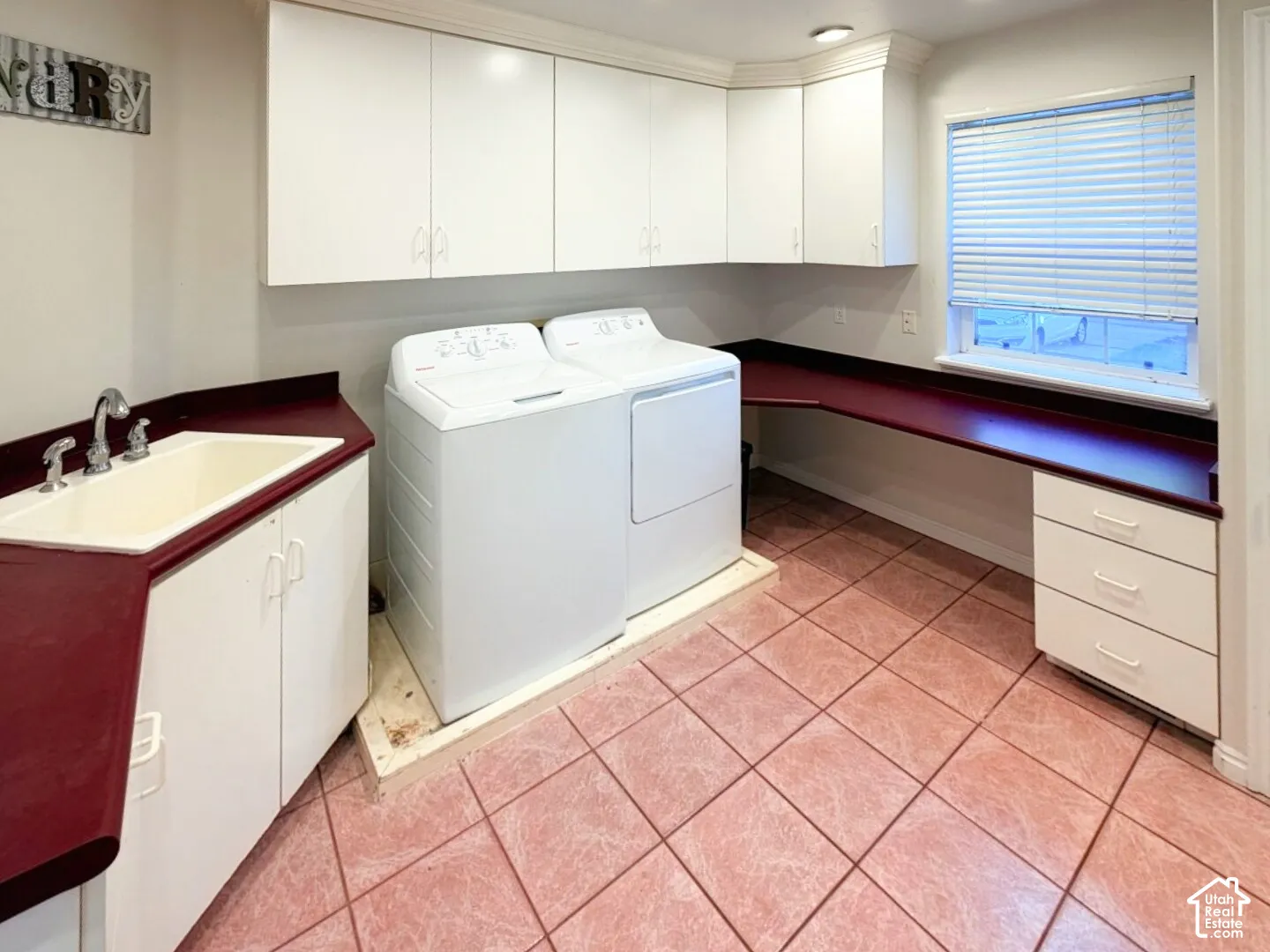 Laundry area featuring wall-mounted white cabinetry, a built-in sink with metal fixtures, a solid-surface countertop, multiple lower storage drawers, and tile flooring