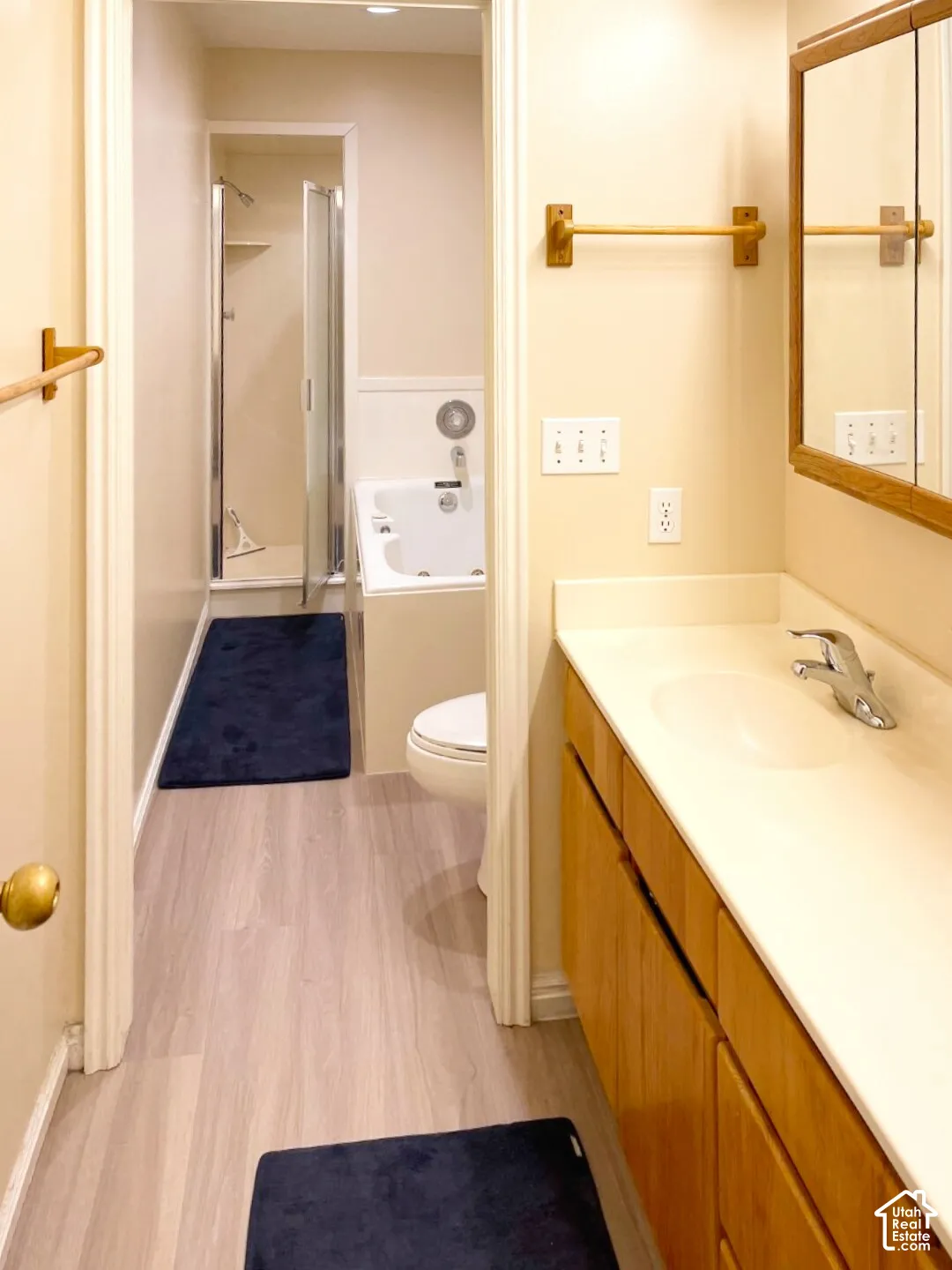 Bathroom featuring wood-finish cabinetry, a solid-surface vanity countertop with an integrated sink, a deep soaking tub, and a separate glass-enclosed shower stall