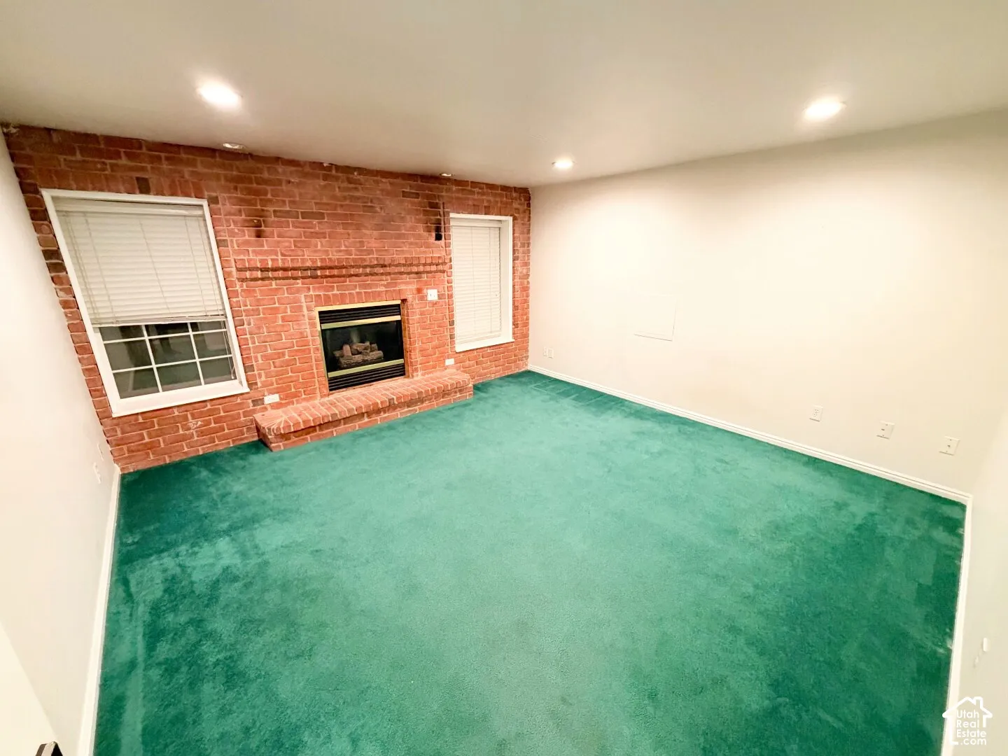 Exposed red brick fireplace with an integrated hearth, recessed lighting, and wall-to-wall carpeting