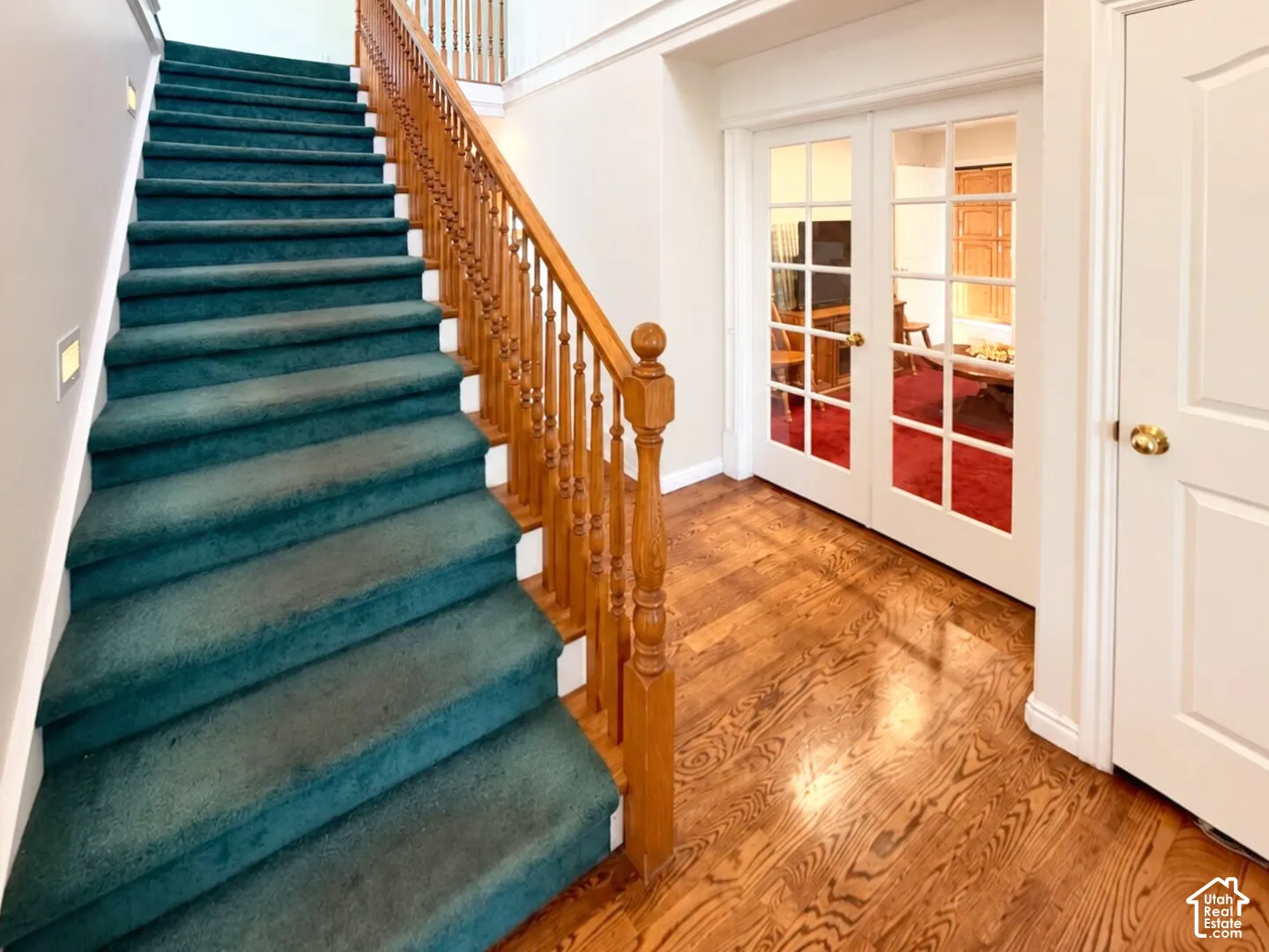 Carpeted staircase with a decorative wood handrail and balusters, wood-finish flooring, and French doors with glass panes