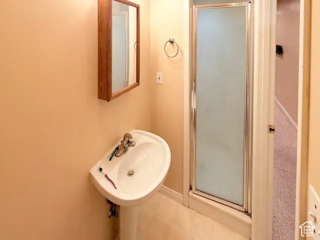 Bathroom featuring a white pedestal sink, single-handle metal faucet, wall-mounted wooden medicine cabinet, and a glass-enclosed shower stall