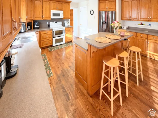 Kitchen featuring wood-finish cabinetry, a tiered center island with bar seating, solid-surface countertops, and wood-finish flooring