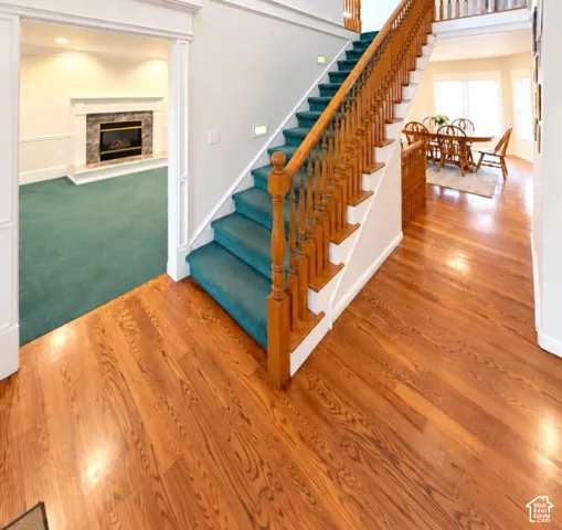 Foyer featuring wood-finish flooring, a staircase with a wooden balustrade, and a fireplace with a stone-surround mantel