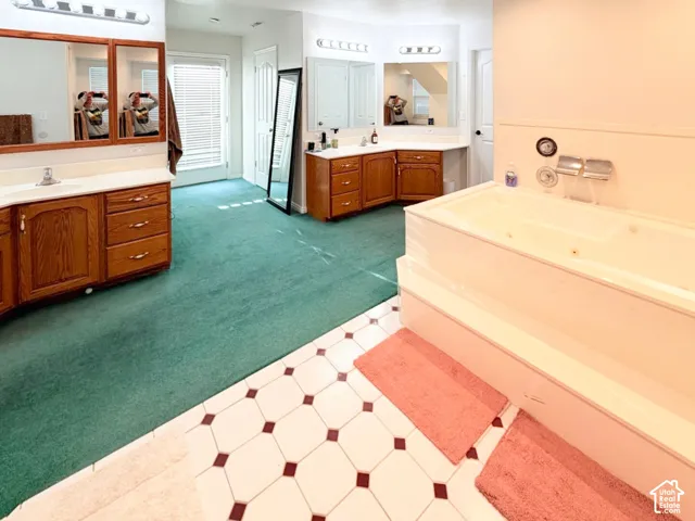 Dual vanity areas featuring wood cabinetry, white countertops, oversized wall-mounted mirrors, and geometric tile flooring with a large built-in soaking tub