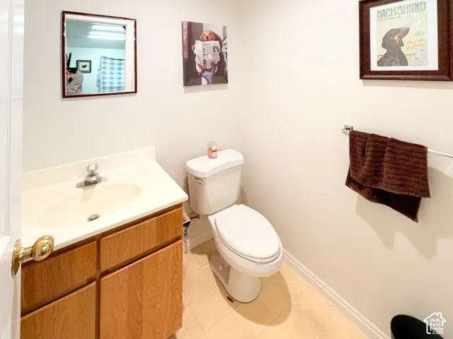 Vanity with integrated sink and countertop, wood-finish cabinetry, porcelain toilet, wall-mounted mirror, and metal towel bar