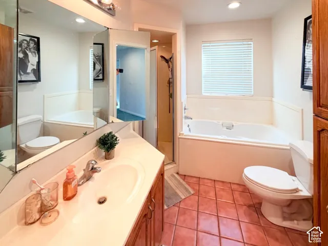 Bathroom featuring a wood-finish vanity with a molded countertop and integrated sink, a deep-soaking garden tub, tile flooring, a large wall-mounted mirror, and a glass-enclosed shower