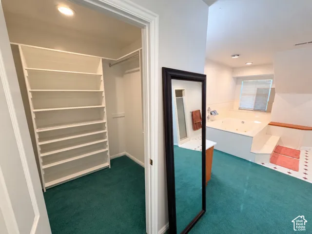 Walk-in closet with built-in shelving, jetted soaking tub with tile surround, and recessed lighting