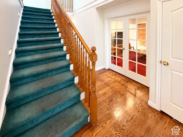 Carpeted staircase with a decorative wood handrail and balusters, wood-finish flooring, and French doors with glass panes
