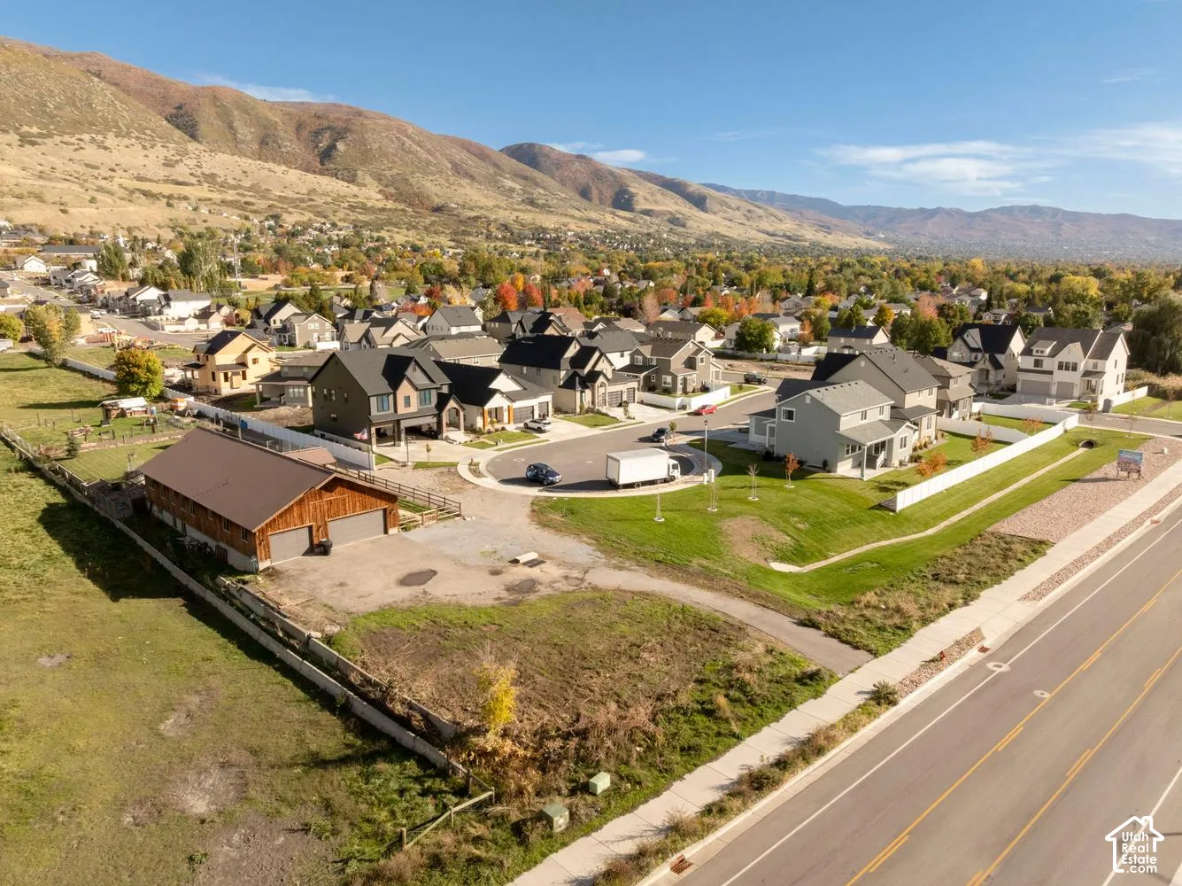 Expansive residential parcel featuring a detached multi-car garage with wood-finish siding, asphalt-shingle roofing, mountainous terrain backdrop, and established street infrastructure
