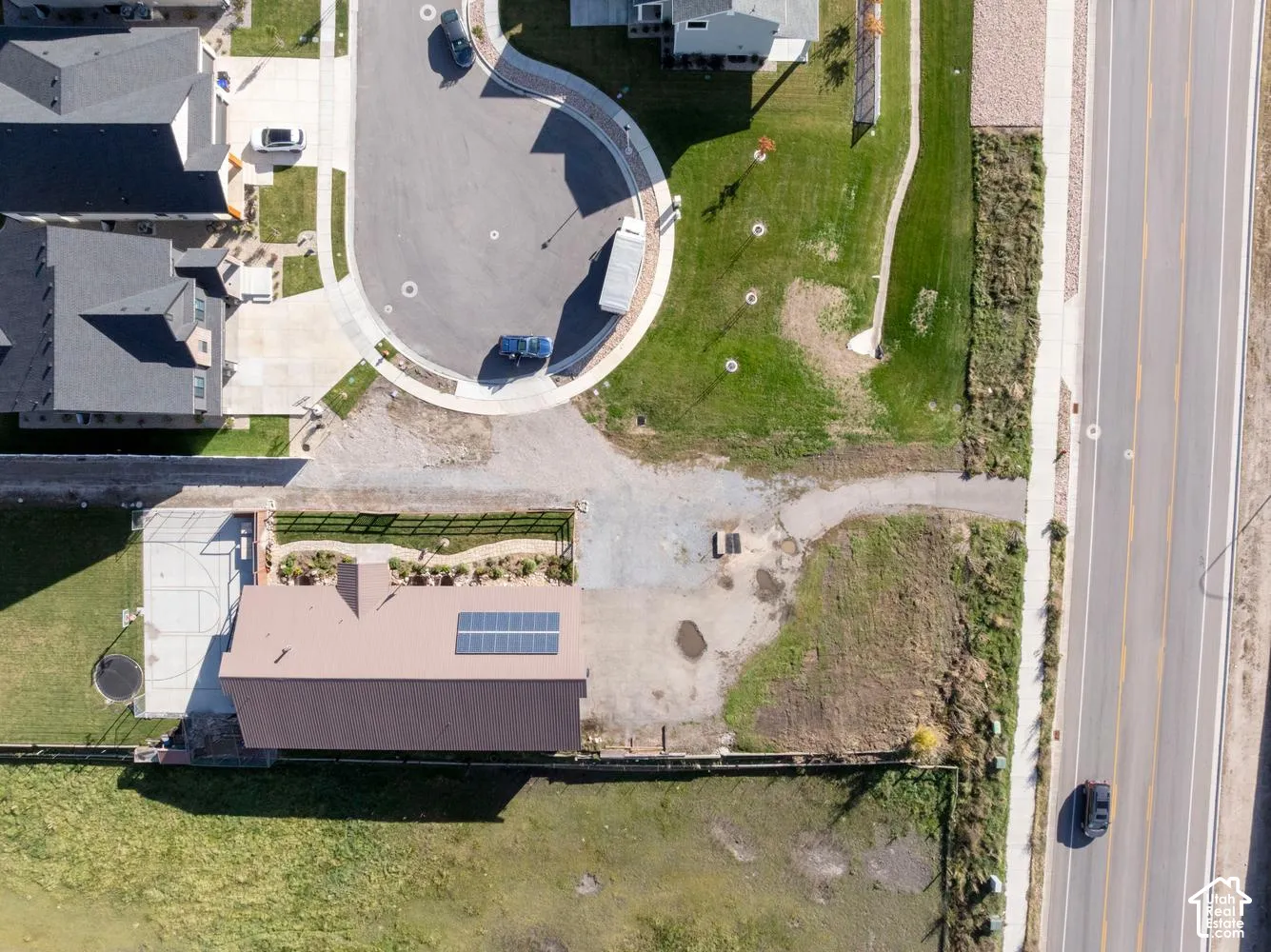 Aerial perspective of property featuring a metal roof with integrated solar panels, a paved sport court, professional landscape beds, and perimeter fencing