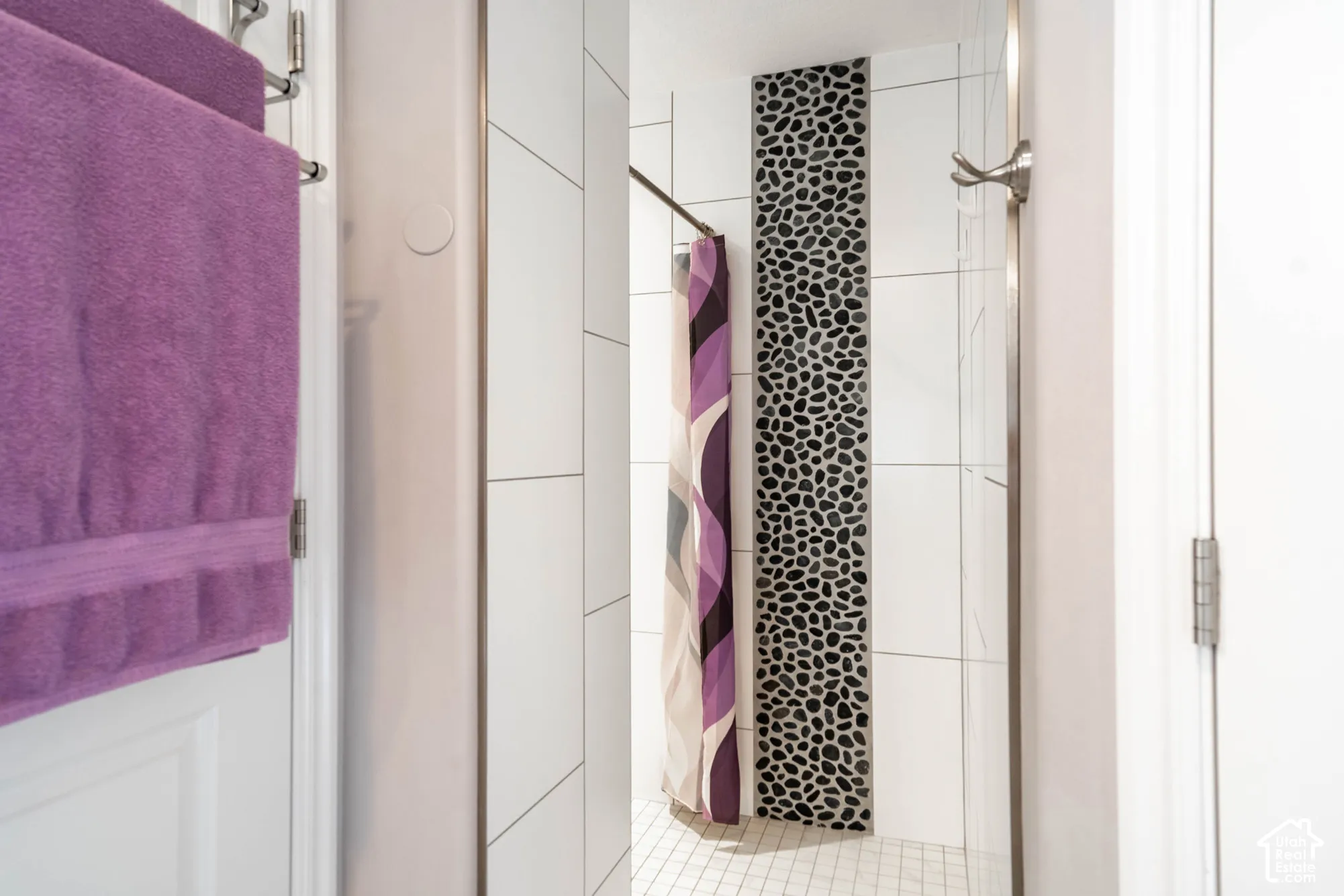 Shower stall featuring large-format white tile, decorative vertical river rock accent inlay, and white mosaic floor tile