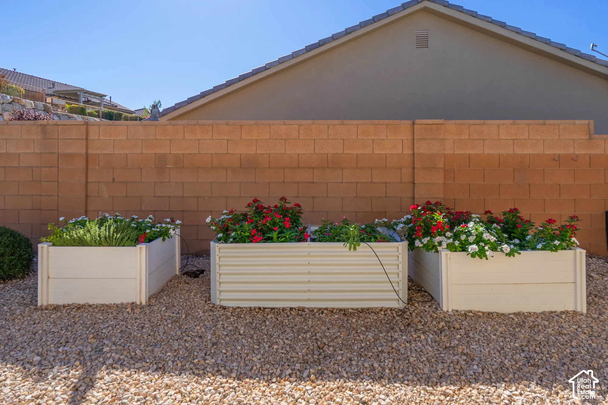 Three raised corrugated metal garden beds featuring stone-aggregate ground cover and a masonry block perimeter wall