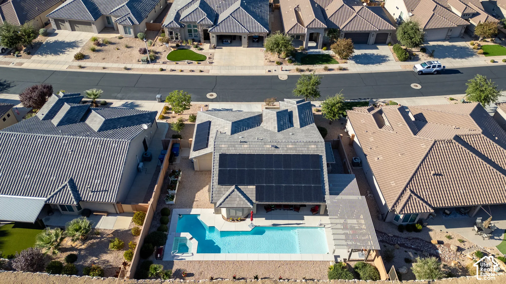 Aerial perspective featuring a shingled roof with installed solar panels, an in-ground pool with integrated spa, and a covered patio area