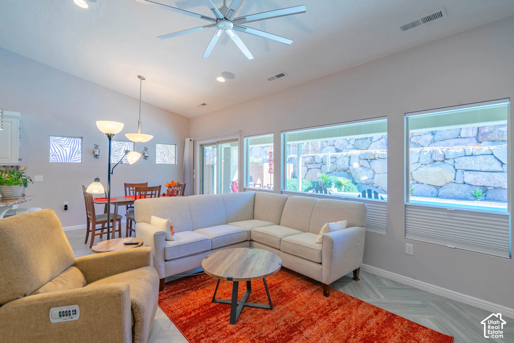 Open-concept living space featuring vaulted ceilings, oversized windows with window treatments, a central ceiling fan, and wood-finish flooring in a herringbone pattern