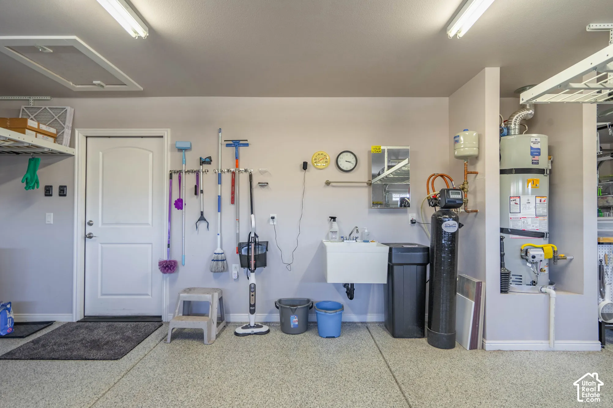 Garage interior featuring finished epoxy flooring, a wall-mounted utility sink, and recessed water heater alcove