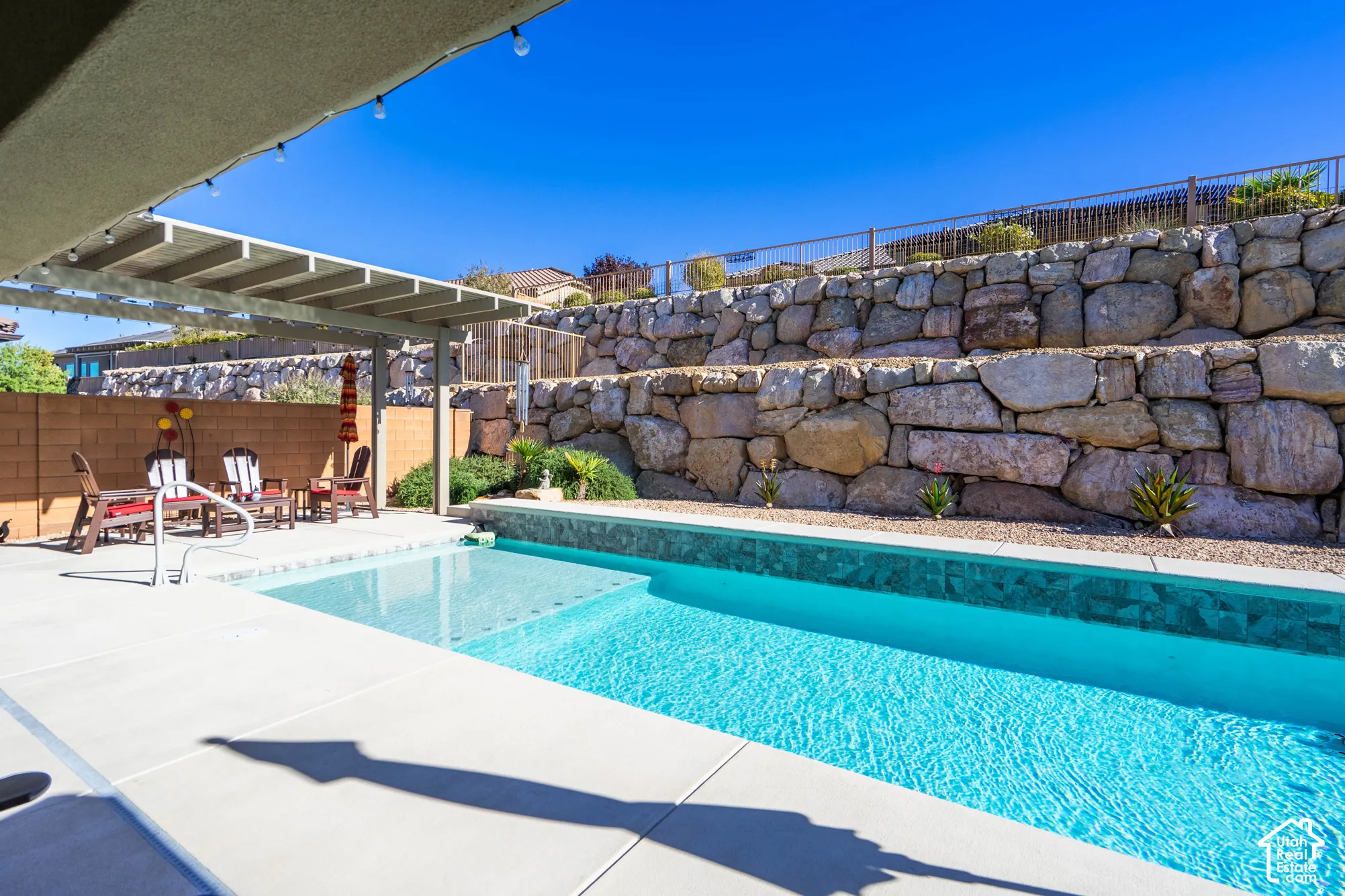 Swimming pool with built-in tanning ledge, covered patio structure, and terraced stone retaining walls