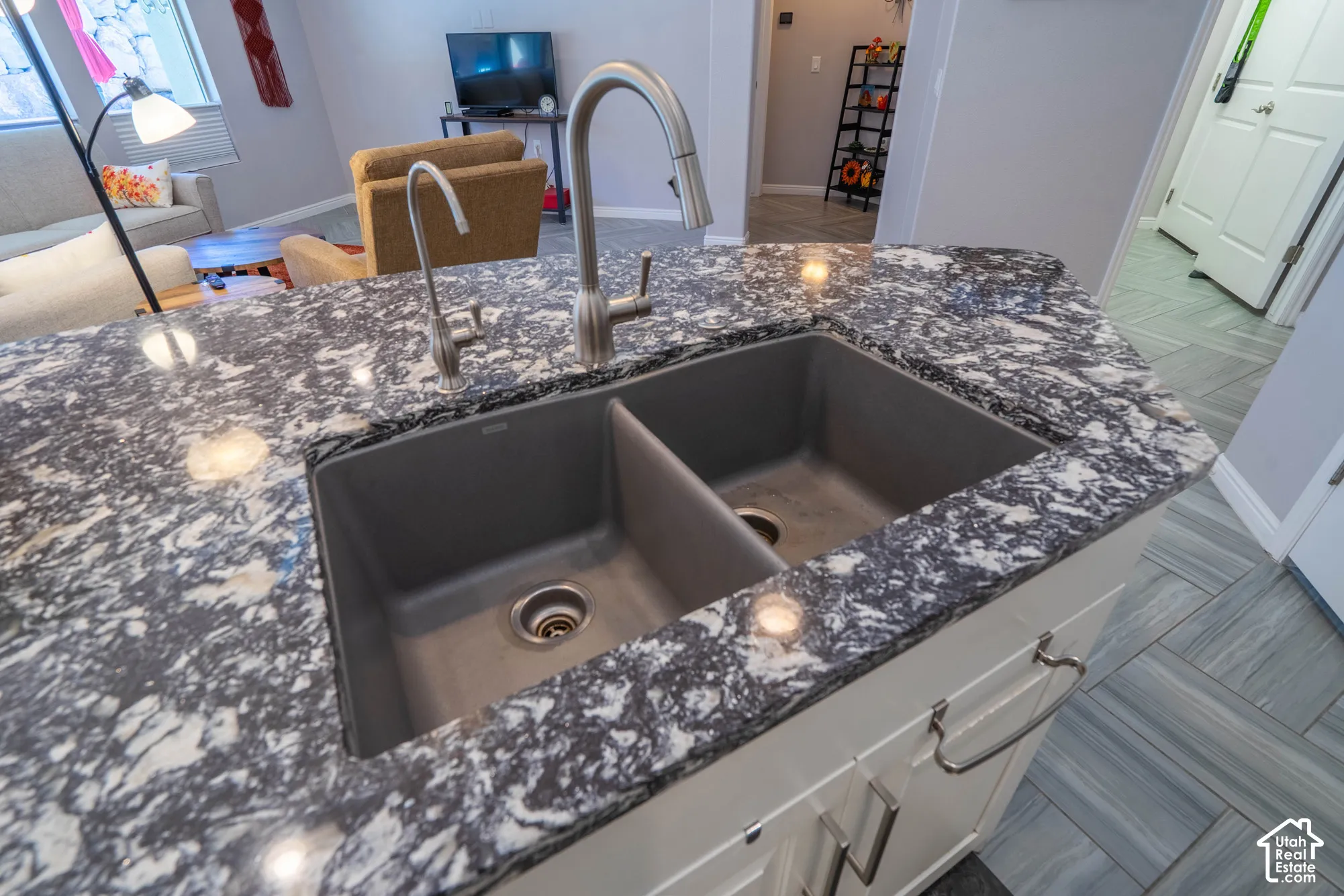 Kitchen island featuring a high-contrast patterned countertop, dual-basin composite sink, stainless steel pull-down faucet, and white cabinetry with brushed-metal pulls