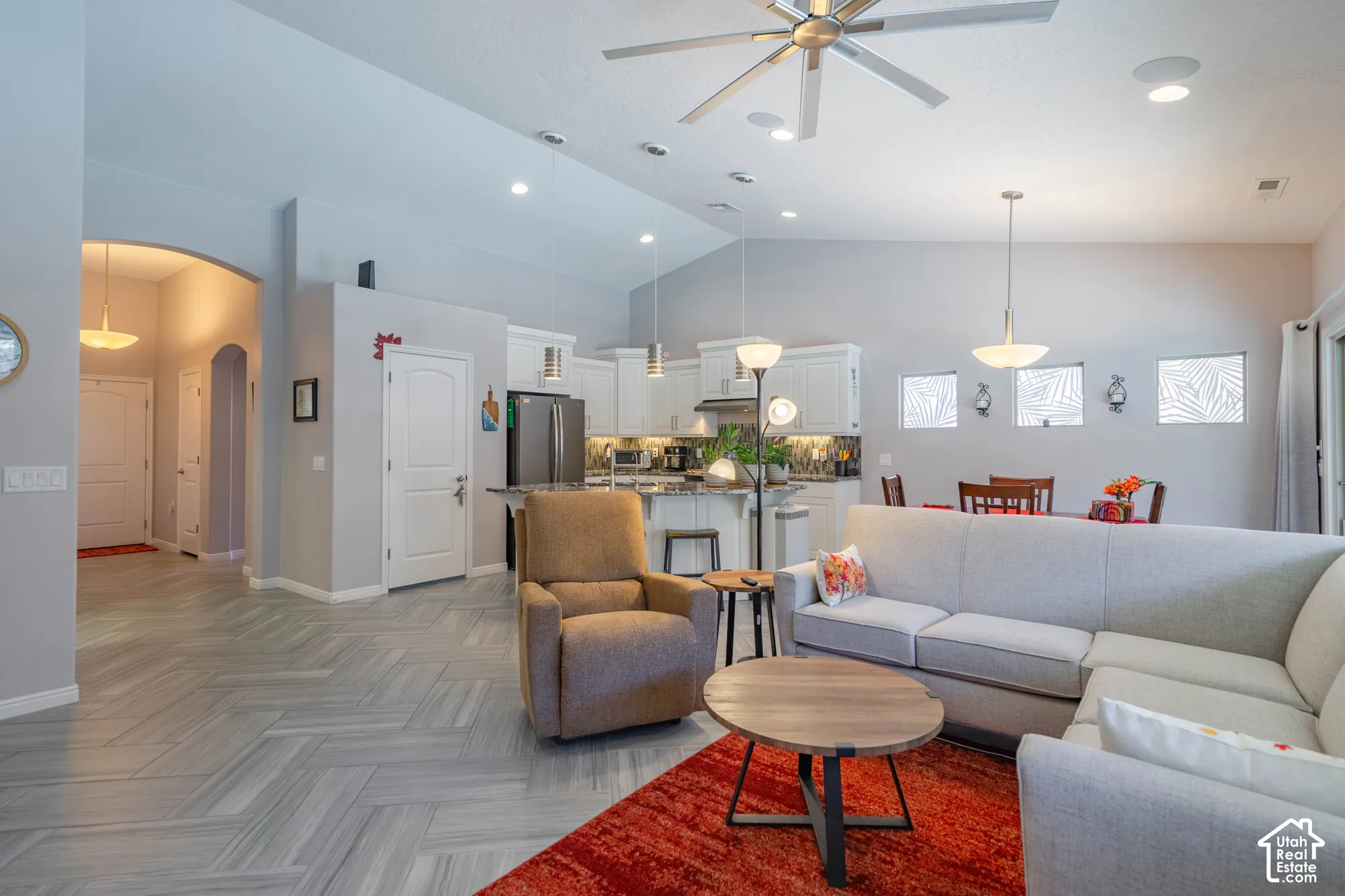 Vaulted ceilings featuring a multi-blade ceiling fan, herringbone-patterned tile flooring, recessed lighting, and a kitchen equipped with white cabinetry and a central island