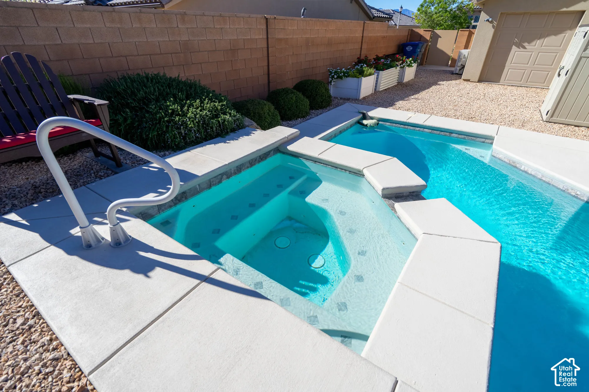 In-ground spa with stone tile accents, swimming pool, concrete deck, gravel landscaping, and concrete block perimeter wall