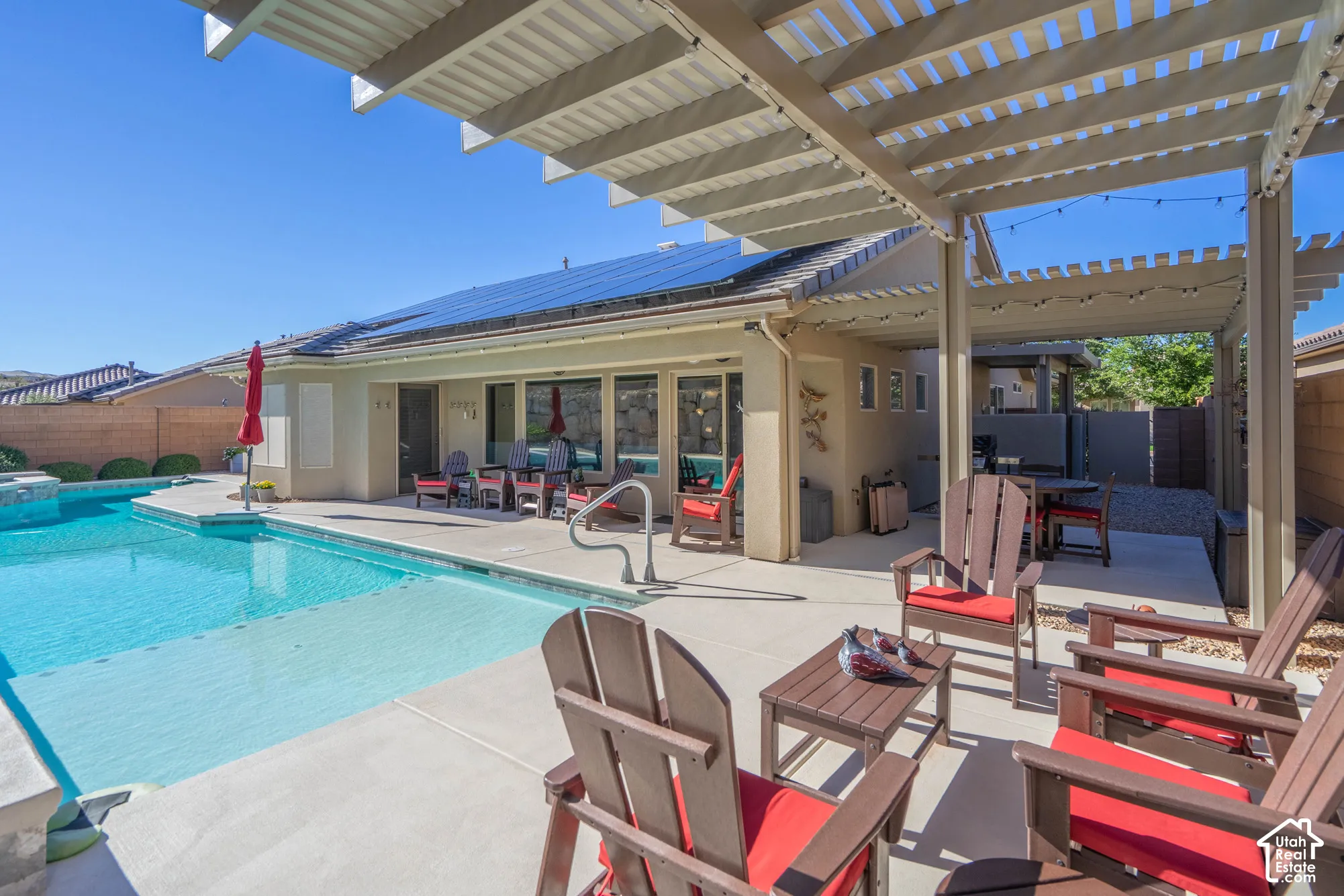 Backyard featuring an in-ground swimming pool, concrete patio, slatted pergola, and rooftop solar panels