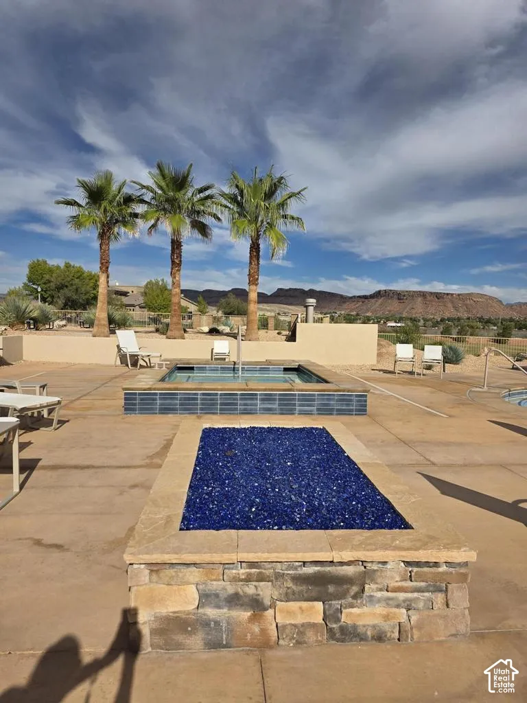 Outdoor patio featuring a built-in fire feature with cobalt blue glass, raised spa with tiled surround, and a concrete deck with a mountain backdrop