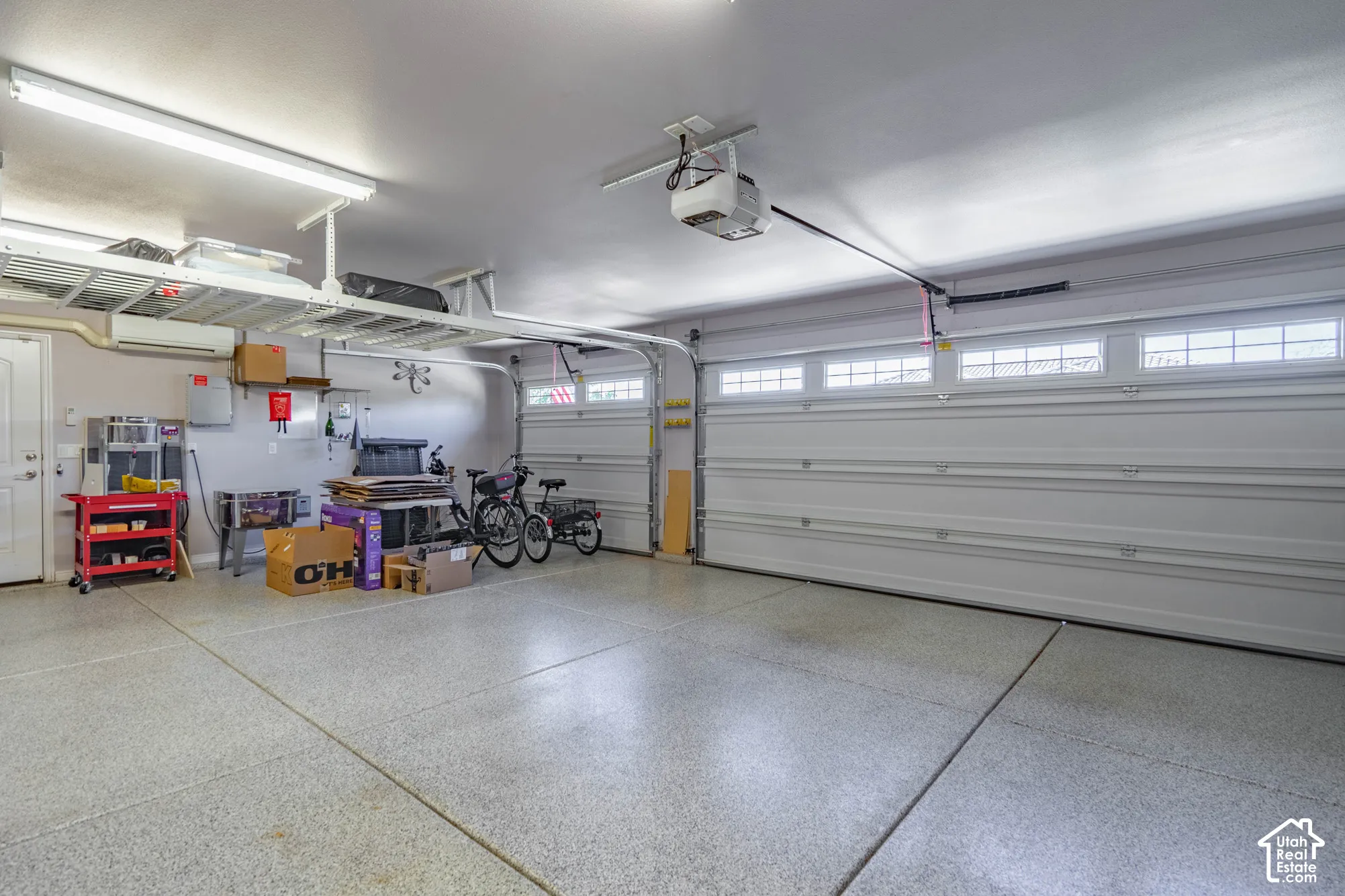 Multi-car garage featuring epoxy-coated flooring, overhead metal storage shelving, integrated ceiling lighting, and sectional garage doors with transom windows