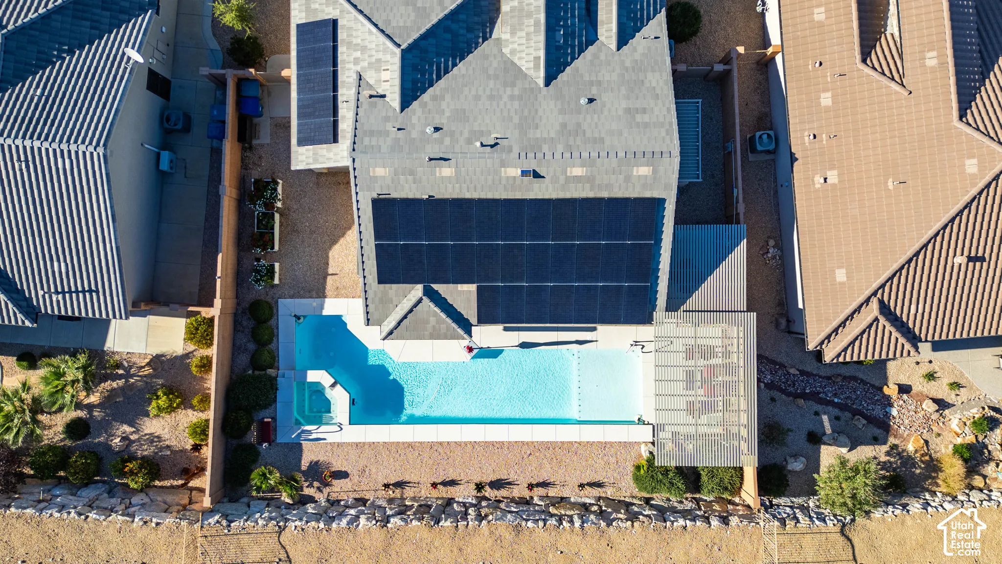 Aerial perspective of property featuring integrated solar panels, an in-ground swimming pool with spa, and a pergola-covered patio area