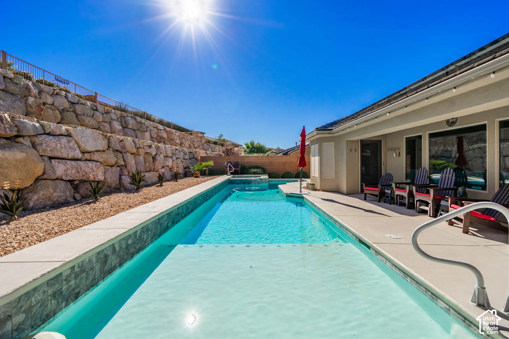 Rectangular swimming pool with integrated spa and decorative tile border, featuring a poured concrete deck and natural stone terraced retaining wall