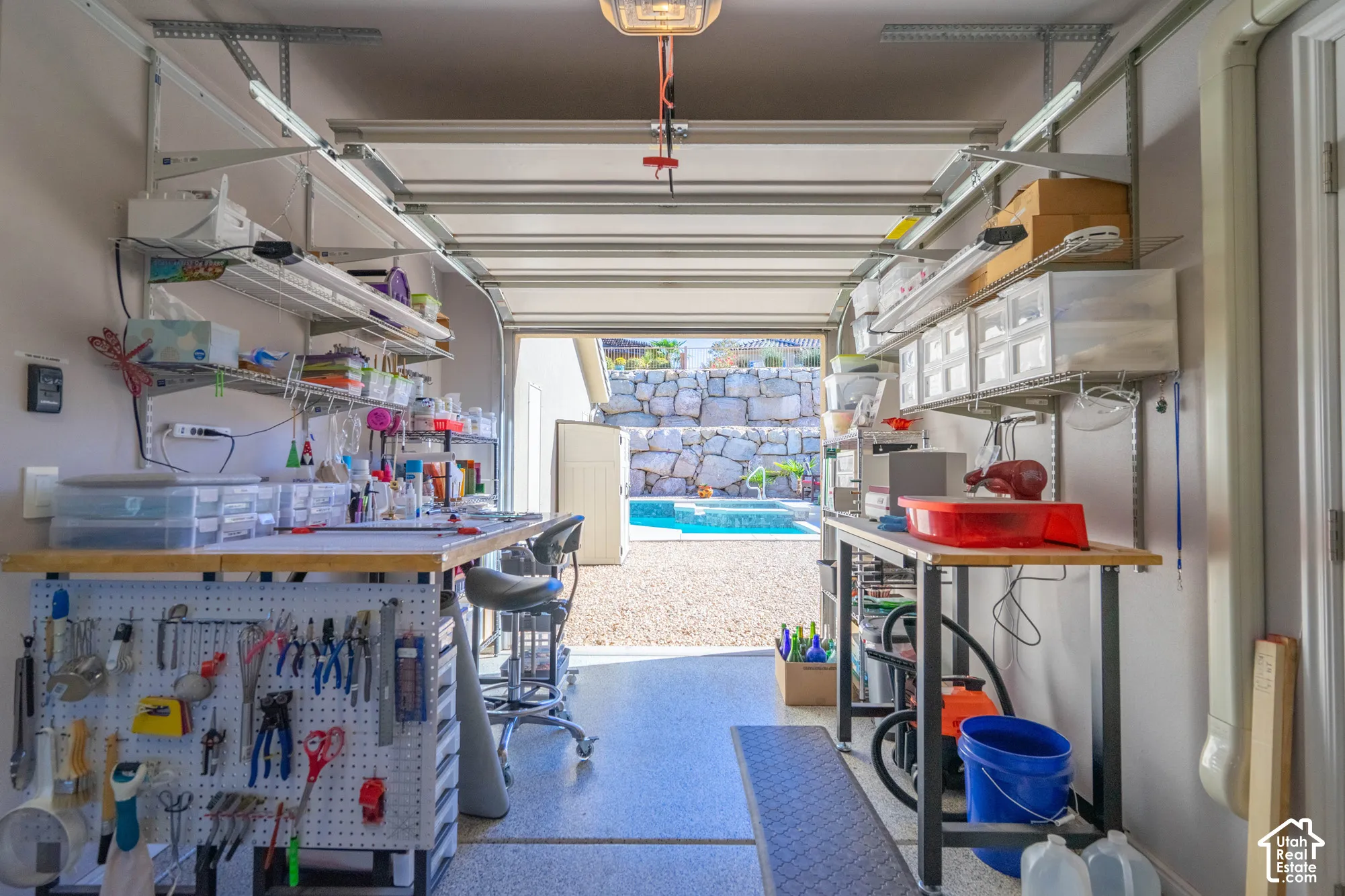 Finished garage featuring epoxy flooring, wall-mounted steel shelving, pegboard organization systems, and integrated overhead lighting.  Extra Roll Up Door into Back Yard