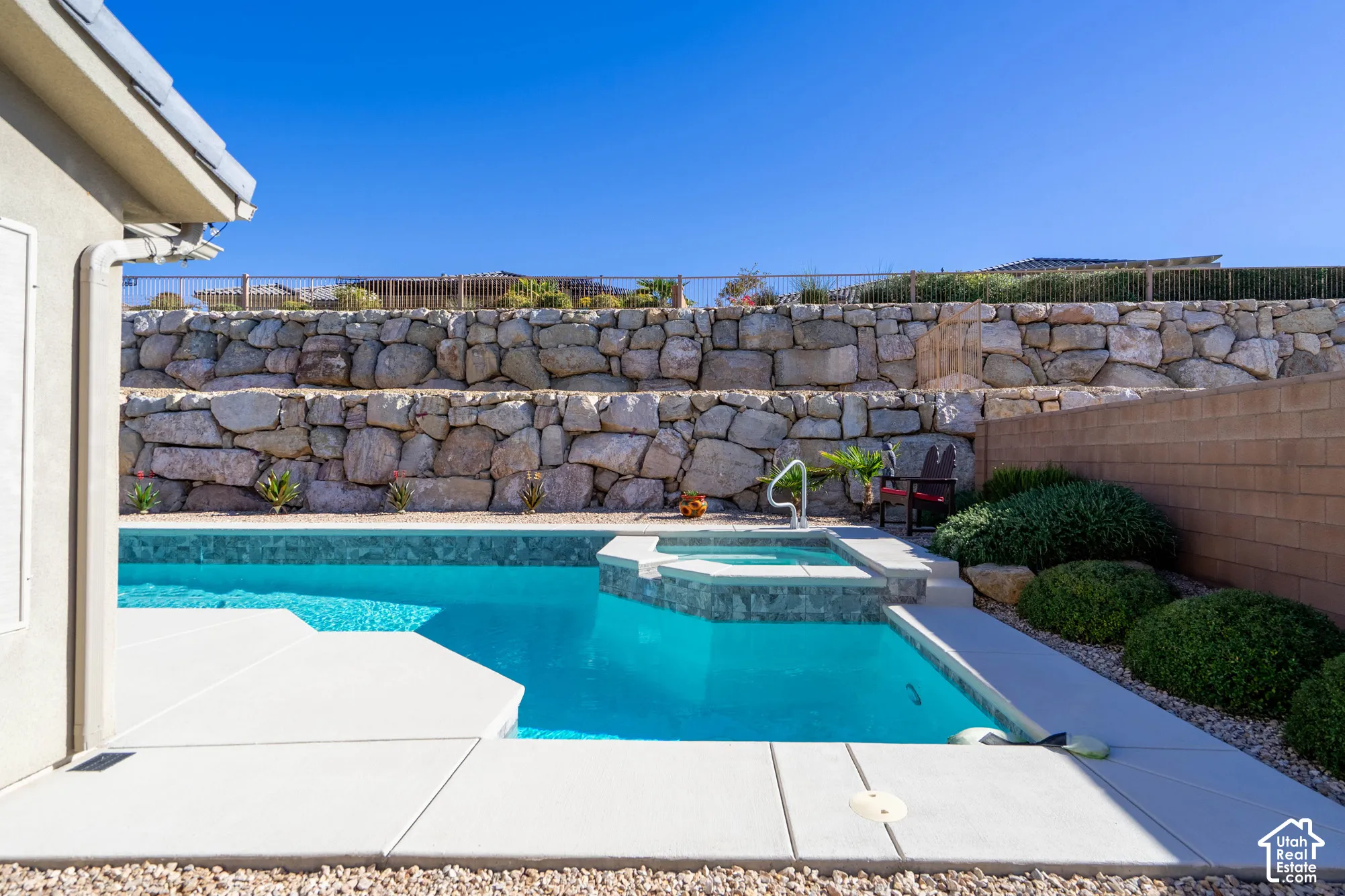 In-ground swimming pool with an integrated spa, concrete deck, terraced stone retaining walls, and rock landscaping
