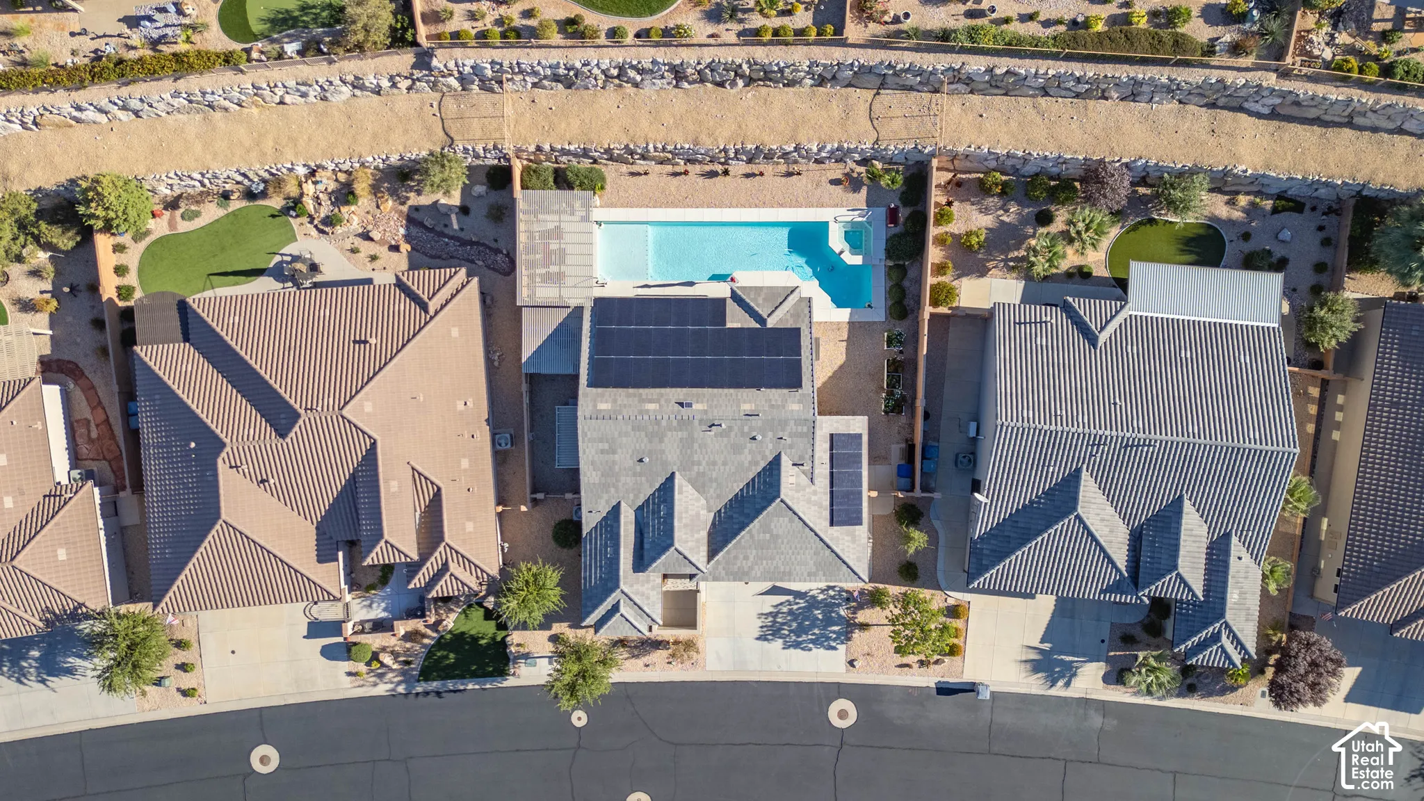 Aerial view featuring a swimming pool, installed solar panels, xeriscaped grounds, and masonry retaining wall