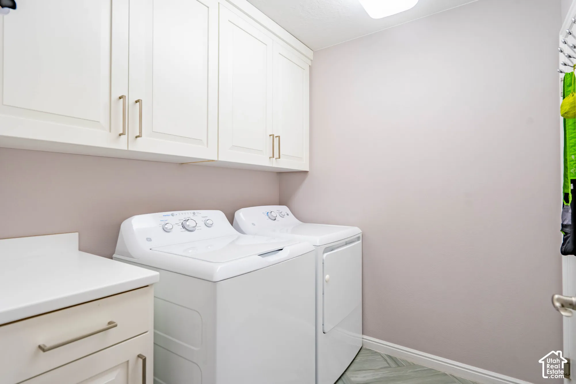 Utility area featuring white shaker-style wall and base cabinetry, solid-surface countertop, and patterned tile flooring