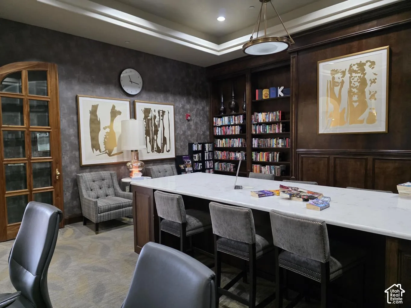 Built-in wood shelving, central island with a stone-surface countertop, recessed tray ceiling, arched glass-panel wood door, and textured wall finish