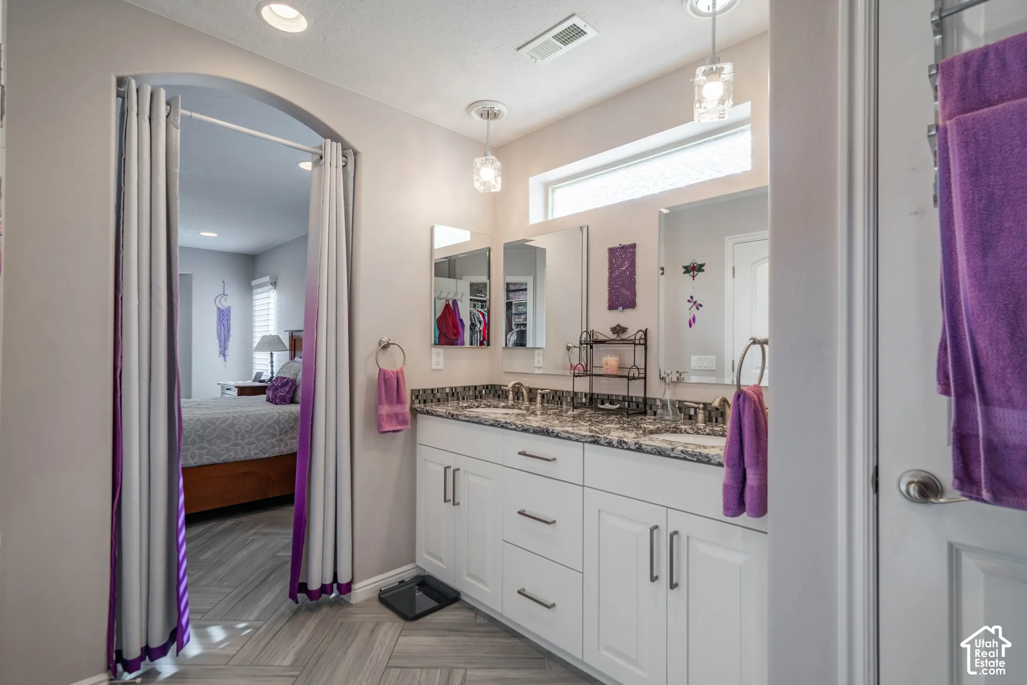 Dual-sink vanity with stone countertop and white cabinetry, complemented by chevron-patterned flooring, arched entryway, and dual hanging pendant lights