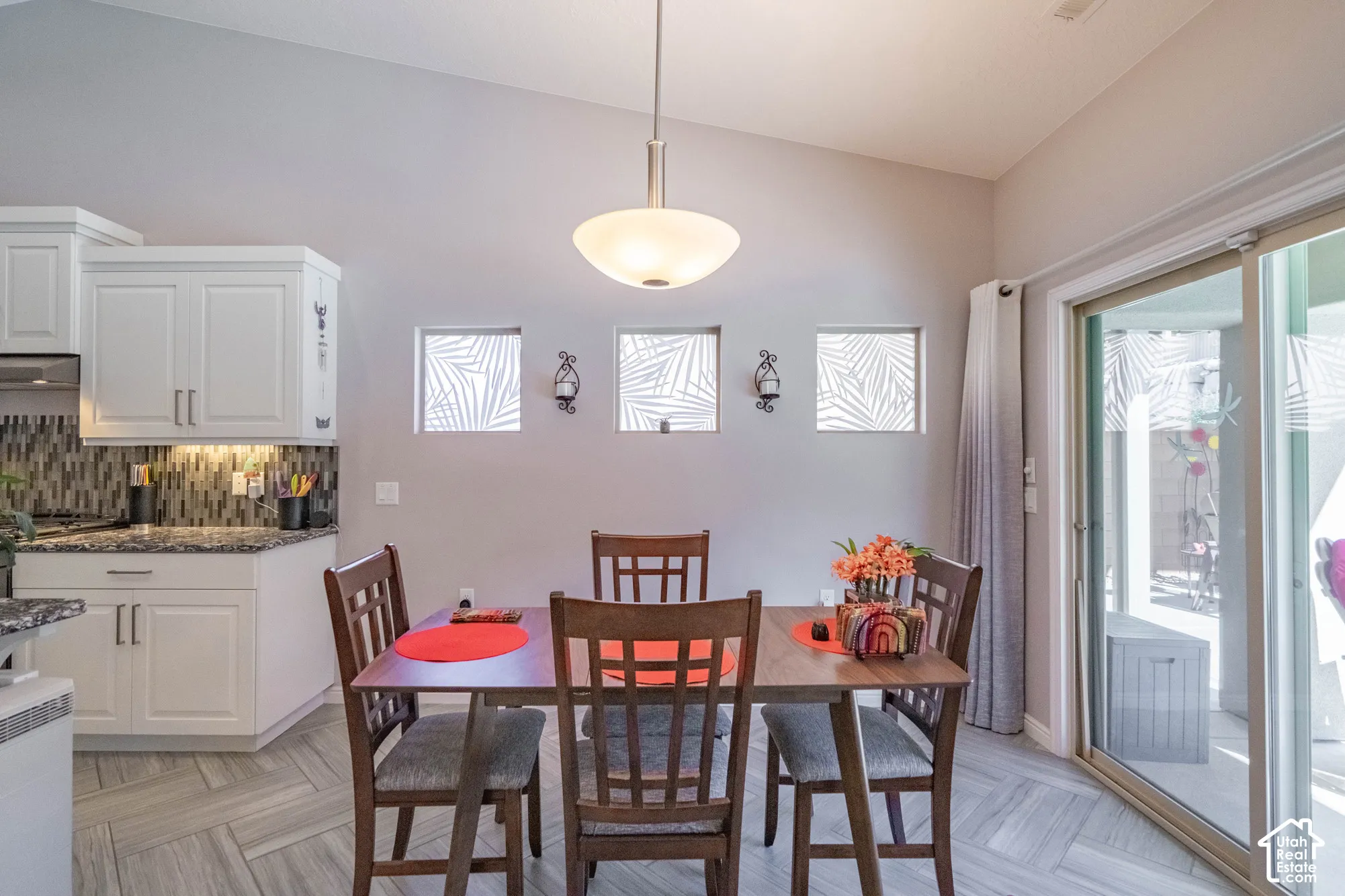 Vaulted ceilings, white cabinetry, decorative tile backsplash, stone-surface countertops, and large sliding glass doors