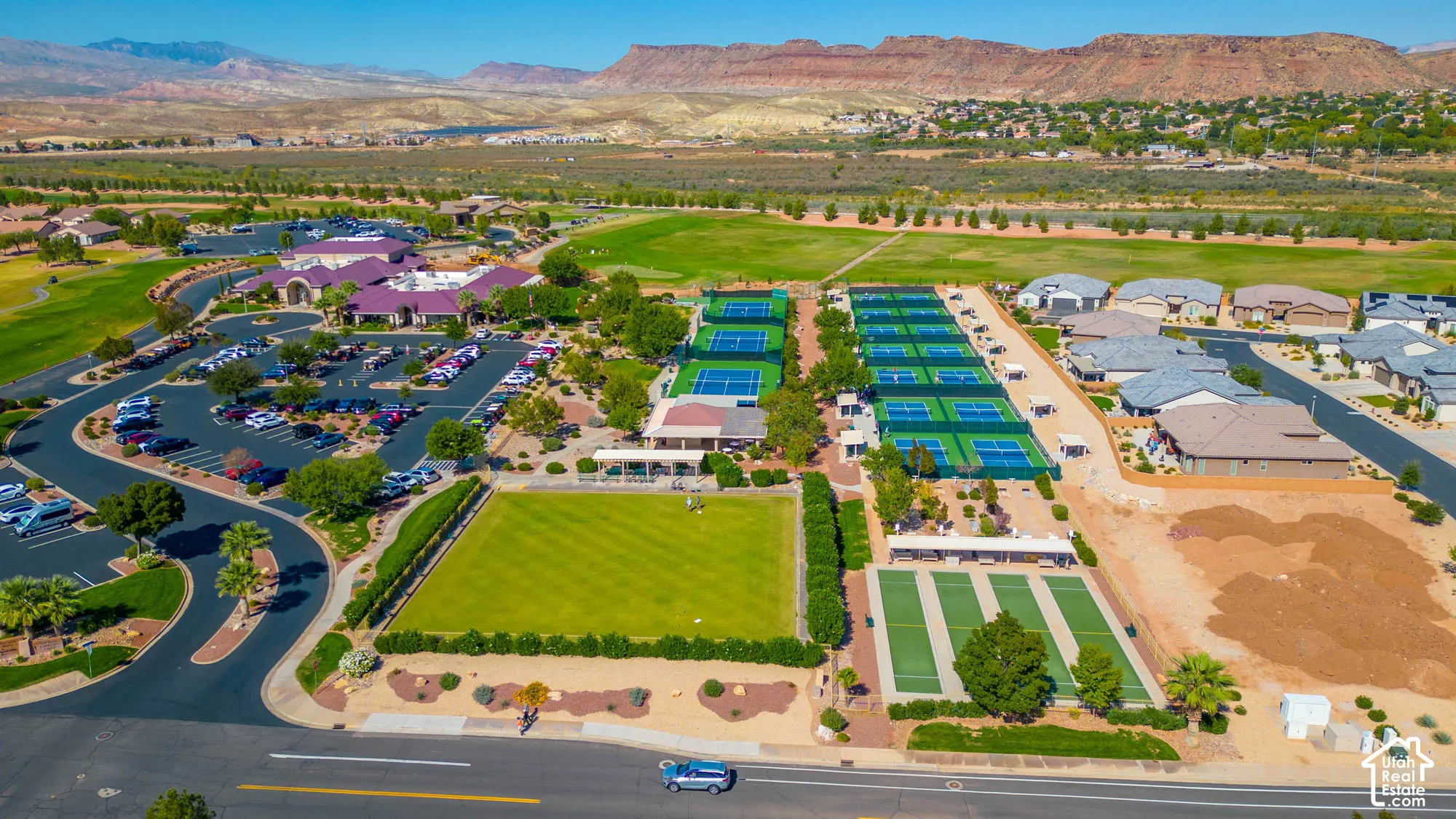 Aerial perspective of community recreation grounds featuring multiple tennis courts, pickleball courts, a manicured lawn, and expansive mountain terrain