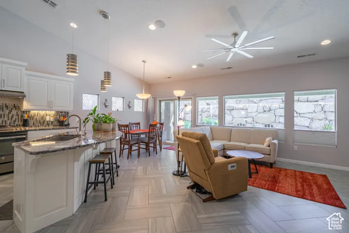 Open-concept interior featuring large-format tile flooring laid in a herringbone pattern, white cabinetry, a multi-tonal tile backsplash, and a multi-blade ceiling fan