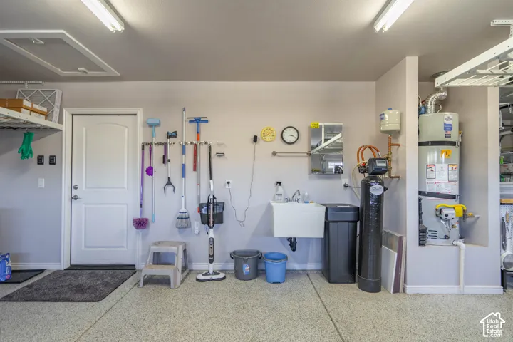 Garage interior featuring finished epoxy flooring, a wall-mounted utility sink, and recessed water heater alcove