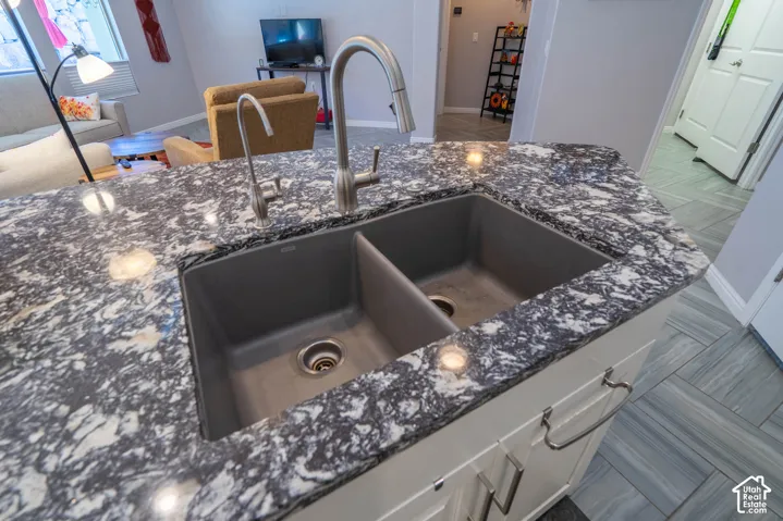 Kitchen island featuring a high-contrast patterned countertop, dual-basin composite sink, stainless steel pull-down faucet, and white cabinetry with brushed-metal pulls