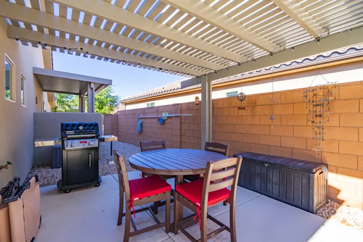 Covered outdoor patio featuring a slatted metal pergola, concrete flooring, and a decorative masonry block wall enclosure