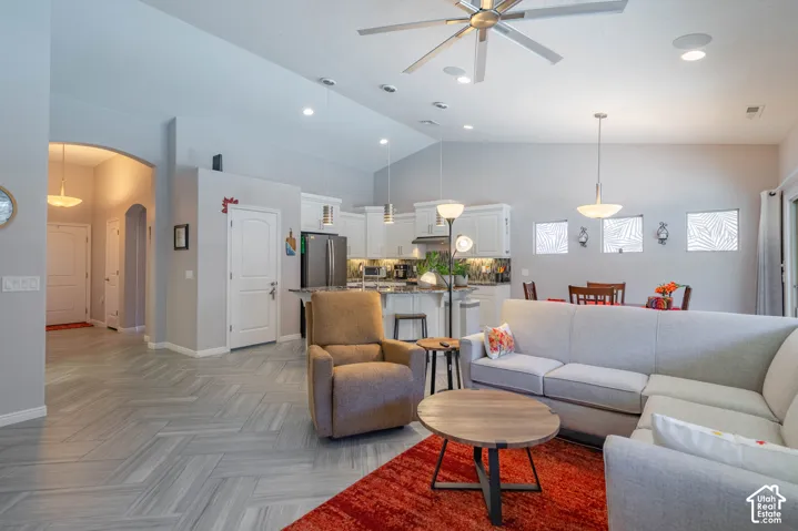 Vaulted ceilings featuring a multi-blade ceiling fan, herringbone-patterned tile flooring, recessed lighting, and a kitchen equipped with white cabinetry and a central island